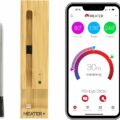 An image of the MEATER Plus, a Bluetooth meat thermometer perfect for any BBQ enthusiast. The wireless device includes a metal probe and a bamboo charging dock. Next to it is a smartphone displaying the MEATER app, showcasing cooking metrics like internal and ambient temperatures and remaining cooking time.