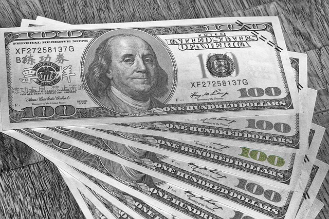 A fanned out stack of U.S. one hundred dollar bills is displayed on a wooden surface. The bills feature a portrait of Benjamin Franklin. The image is in grayscale, which removes all color from the scene—an inspiration for anyone looking to sell photos online and make money through their creative work.